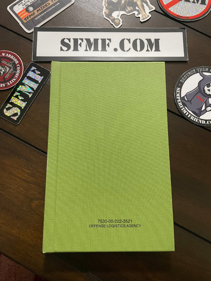 Green hard cover notebook with a label indicating 'SFMF.COM', placed on a table with various items in the background.